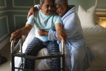 Старша афроамериканська пара сидить на ліжку, обіймаючись у спальному приміщенні. Життя на пенсії в самоізоляції під час коронавірусної ковини 19 пандемії. — стокове фото