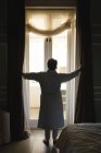 Mujer afroamericana mayor parada junto a una ventana en un dormitorio. estilo de vida de jubilación en aislamiento durante el coronavirus covid 19 pandemia. - foto de stock