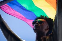 Hombre de raza mixta parado en la azotea sosteniendo la bandera del arco iris. género fluido lgbt identidad concepto de igualdad racial. - foto de stock