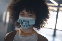 Femme de race mixte portant un masque facial avec slogan regardant la caméra. genre fluide identité lgbt concept d'égalité raciale. — Photo de stock