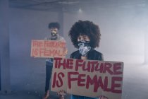 Homem e mulher de raça mista usando máscaras faciais segurando sinais de protesto. gênero fluido lgbt identidade conceito de igualdade racial. — Fotografia de Stock