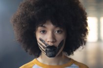 Femme de race mixte ayant une impression de main noire peinte sur le visage regardant la caméra. genre fluide identité lgbt concept d'égalité raciale. — Photo de stock