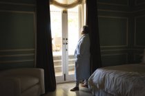 Старша афро-американська жінка стоїть біля вікна у спальній кімнаті. Життя на пенсії в самоізоляції під час коронавірусної ковини 19 пандемії. — стокове фото