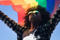 Mixed race woman standing on rooftop holding rainbow flag. gender fluid lgbt identity racial equality concept. — Stock Photo