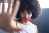 Femme de race mixte avec ruban adhésif sur la bouche regardant la caméra tenant son bras droit. genre fluide identité lgbt concept d'égalité raciale. — Photo de stock