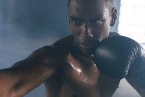Um afro-americano a usar luvas de boxe a bater num saco de boxe num edifício urbano vazio. fitness urbano estilo de vida saudável. — Fotografia de Stock