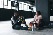 Afroamerikaner sitzen in einem leer stehenden städtischen Gebäude und ruhen sich aus, nachdem sie Basketball gespielt haben. Wasser trinken und reden. urbane Fitness gesunder Lebensstil. — Stockfoto