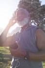 Se adapta al hombre afroamericano mayor sosteniendo un teléfono inteligente poniéndose auriculares. saludable retiro tecnología comunicación al aire libre fitness estilo de vida. - foto de stock