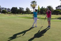 Due donne caucasiche che giocano a golf, una che toglie la bandiera dal buco. sport tempo libero hobby golf sano stile di vita all'aperto. — Foto stock