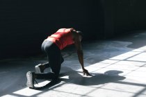 Африканський американець у спортивному одязі на колінах починає працювати у порожньому міському будинку. Здоровий спосіб життя в місті. — стокове фото
