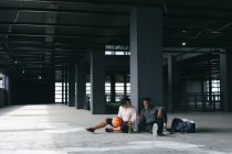 Африканський американець і жінка сидять у порожньому міському будинку і відпочивають після гри в баскетбол. за допомогою смартфона і сміху. Здоровий спосіб життя в місті. — стокове фото