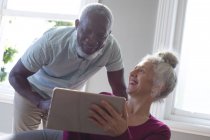 Senioren-Mixed-Race-Paar sitzt auf der Couch und schaut gemeinsam auf das digitale Tablet im Wohnzimmer. Während der Quarantäne zu Hause bleiben und sich selbst isolieren. — Stockfoto