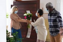Senior african american couple greeting senior caucasian couple all wearing face masks at home. health hygiene wellbeing at senior care home during coronavirus covid 19 pandemic. — Stock Photo