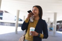 African american woman with coffee cup talking on smartphone on the street. lifestyle living during coronavirus covid 19 pandemic. — Stock Photo