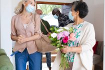 Coppia afroamericana anziana che saluta la coppia caucasica anziana indossando tutti maschere facciali a casa. salute igiene benessere a casa di cura durante coronavirus covid 19 pandemia. — Foto stock