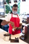 Portrait of african american male barista wearing face mask using coffee machine looking at camera. health and hygiene in business during coronavirus covid 19 pandemic. — Stock Photo