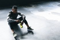 Homem afro-americano sentado em prédio urbano vazio e descansando depois de jogar basquete. segurando uma garrafa de água. fitness urbano estilo de vida saudável. — Fotografia de Stock