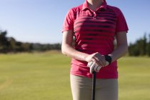 Sección media de la mujer de pie en el campo de golf que sostiene el club de golf. deporte ocio aficiones golf estilo de vida al aire libre saludable. - foto de stock