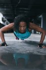 Mujer afroamericana con ropa deportiva haciendo flexiones en un edificio urbano vacío. aptitud urbana estilo de vida saludable. - foto de stock