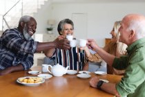 Старші кавказькі та афро-американські пари сидять за столом і п'ють чай удома. Друзі на пенсії.. — стокове фото