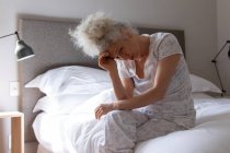 Mulher caucasiana sênior sentando-se fraca na cama. ficar em casa em auto-isolamento durante o confinamento de quarentena. — Fotografia de Stock