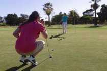Zwei kaukasische Frauen spielen Golf, eine hockt, bevor sie einen Schuss auf das Loch abfeuern. Sport Freizeit Hobbys Golf gesunder Lebensstil im Freien. — Stockfoto
