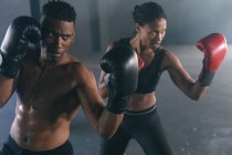 Un homme et une femme afro-américains portant des gants de boxe jetant des coups de poing dans l'air dans un bâtiment vide. forme physique urbaine mode de vie sain. — Photo de stock