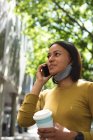 African american woman with lowered face mask talking on smartphone on the street. lifestyle living concept during coronavirus covid 19 pandemic. — Stock Photo