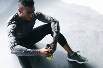 Afroamerikaner sitzt in einem leeren städtischen Gebäude und ruht sich aus, nachdem er Basketball gespielt hat. mit einer Flasche Wasser in der Hand. urbane Fitness gesunder Lebensstil. — Stockfoto