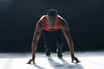 Uomo afroamericano con indosso vestiti sportivi inginocchiati che iniziano a correre in un edificio urbano vuoto. fitness urbano stile di vita sano. — Foto stock