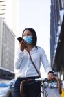 African american woman wearing face mask with bicycle talking on smartphone on the street. lifestyle living concept during coronavirus covid 19 pandemic. — Stock Photo