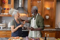 Ein älteres gemischtes Paar steht in der Küche und schneidet Gemüse. Während der Quarantäne zu Hause bleiben und sich selbst isolieren. — Stockfoto