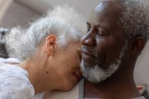 Старшая смешанная расовая пара в спальне, сидящая на кровати обнимаясь. оставаться дома в изоляции во время карантинной изоляции. — стоковое фото