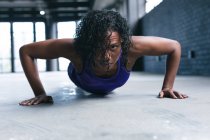 Donna afroamericana che indossa vestiti sportivi facendo flessioni in un edificio urbano vuoto. fitness urbano stile di vita sano. — Foto stock