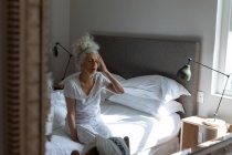 Eine ältere kaukasische Frau fühlt sich schwach, wenn sie im Bett sitzt. Während der Quarantäne zu Hause bleiben und sich selbst isolieren. — Stockfoto
