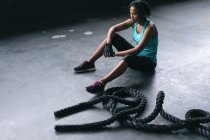 Donna afroamericana che indossa vestiti sportivi seduta a riposo dopo aver combattuto corde in un edificio urbano vuoto. fitness urbano stile di vita sano. — Foto stock