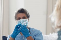 Doctora afroamericana mayor que usa mascarilla para preparar la vacunación en casa. protección de la higiene sanitaria durante la pandemia del coronavirus covid 19. - foto de stock