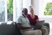 Senior coppia di razza mista seduto sul divano guardando computer portatile insieme in soggiorno. stare a casa in isolamento durante l'isolamento in quarantena. — Foto stock