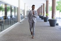 African american male businessman walking wearing face mask talking on smartphone. businessman on the go out in the city. — Stock Photo
