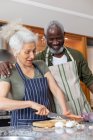 Senior mixed race couple standing in kitchen cutting vegetables. staying at home in self isolation during quarantine lockdown. — Stock Photo
