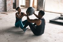 Африканський американець і жінка, які займаються фізичними вправами з м'ячем для ліків у порожньому міському будинку. Здоровий спосіб життя в місті. — стокове фото