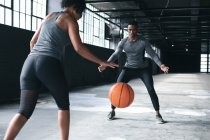 Hombre y mujer afroamericanos de pie en un edificio urbano vacío y jugando baloncesto. aptitud urbana estilo de vida saludable. - foto de stock
