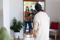 Ein älteres afrikanisch-amerikanisches Paar begrüßt ein älteres kaukasisches Paar, das zu Hause Gesichtsmasken trägt. Gesundheitshygiene Wohlbefinden in Altenheim während Coronavirus Covid 19 Pandemie. — Stockfoto