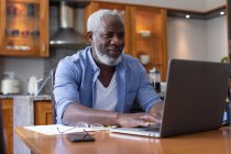 Un anziano afroamericano che usa un portatile per pagare le bollette in sala da pranzo. stare a casa in isolamento durante l'isolamento in quarantena. — Foto stock