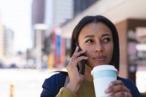 Donna afroamericana con tazza di caffè che parla su smartphone per strada. stile di vita durante il coronavirus covid 19 pandemia. — Foto stock