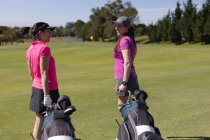 Two caucasian women walking across golf course talking pulling golf bags on wheels. sport leisure hobbies golf healthy outdoor lifestyle. — Stock Photo