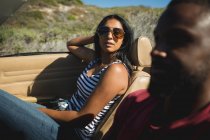 Couple diversifié conduisant sur une journée ensoleillée en voiture convertible parler et sourire. Road trip estival sur une autoroute de campagne au bord de la côte. — Photo de stock