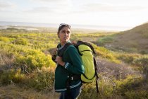 Femme de race mixte portant un sac à dos et randonnée en montagne au bord de la côte. L'été voyage sur une autoroute de campagne au bord de la côte. — Photo de stock