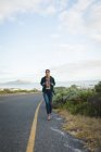 Donna razza mista indossa uno zaino ed escursioni in montagna lungo la costa. L'estate viaggia su un'autostrada di paese dalla costa. — Foto stock