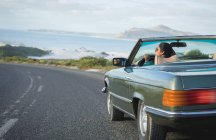 Misto corsa donna alla guida in giornata di sole in auto convertibile tenendo volante. Viaggio estivo su un'autostrada di campagna lungo la costa. — Foto stock